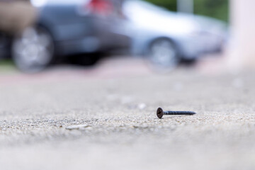 Rusty nails scattered or screw on the road surface in a parking area with cars in the background. Dangerous metal objects on the street that can puncture tires, cause flat tires, vehicle damage.