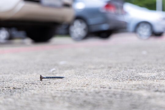 Rusty nails scattered or screw on the road surface in a parking area with cars in the background. Dangerous metal objects on the street that can puncture tires, cause flat tires, vehicle damage.