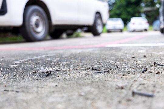 Rusty nails scattered or screw on the road surface in a parking area with cars in the background. Concept of road hazard, traffic safety, and car maintenance risk vehicle damage, or road accidents.