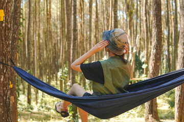 Excited young Asian woman sitting on a hammock while enjoying the forest scenery.