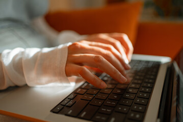 Close-up of female hands typing on laptop keyboard, working remotely from home office, bathed in...