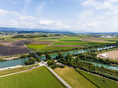 Aerial view of the green fields meeting the flowing river and roads under a vast sky, showcasing a blend of nature and infrastructure, Aare, Switzerland.