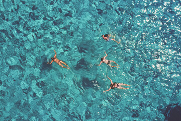 Aerial view of swimmers floating in the crystal-clear turquoise waters, sunlight dancing on the surface, creating a mesmerizing mosaic of light and shadow, Sicily, Italy.