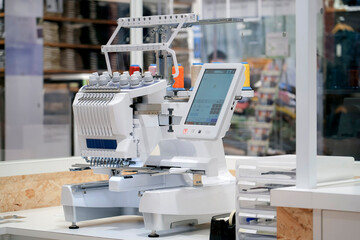 An embroidery machine rests on a table, with a digital display screen. It is positioned within a...