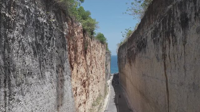 Aerial view of the road snaking between Tebing Panjang Pandawa's monumental cliffs towards the ocean, contrasting textures and tones, Tebing Panjang Pandawa, Bali, Indonesia.