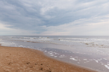 Sandy beach with foamy waves under cloudy sky, Netherlands