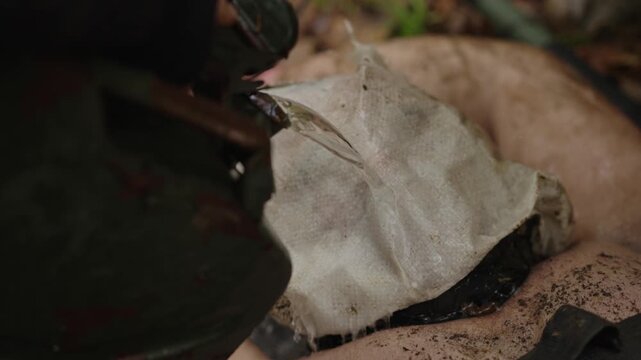 Waterboarding interrogation with hooded, restrained man on forest ground