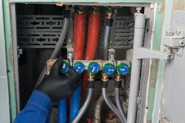 a hand in a black glove closes a cold water tap in a plumbing system