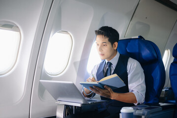 Businessman working on a laptop with documents during a first-class flight. Perfect for themes of...