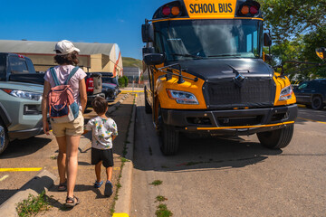 Mother and son walking towards school bus in parking lot