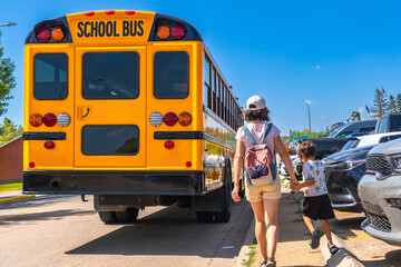 Mother and son walking towards school bus on first day back to school