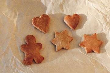 Christmas food still life. Winter composition of star, heart shaped gingerbread cookies, gingerbread man on brown wrinkled baking paper texture background in sunlight. Flat lay, top view. No people