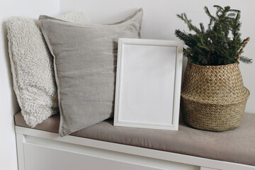 White blank wooden frame mockup. Christmas spruce tree branches in basket. Linen and teddy cushions on beige bench. Poster product display. Scandinavian festive winter home decor, nordic design.