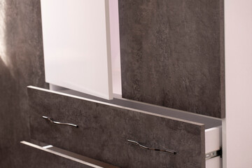Close-up of the drawers of the cabinet with grey cement structure fronts and a white half-open door...