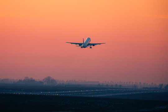 Traffic at airport at golden sunset. Wide shot of passenger airplane taking off from runway.