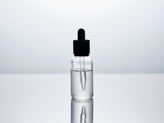 Transparent glass bottle with dropper containing hyaluronic acid serum reflecting on white...