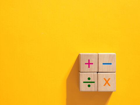 Four wooden cubes showing basic mathematical operations on yellow background