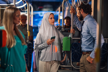 Muslim woman wearing hijab using smartphone on bus while talking to businessman