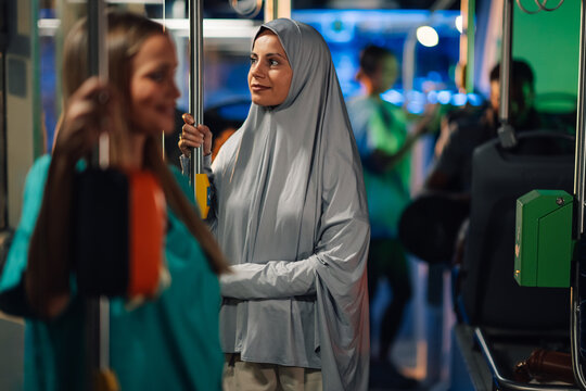Muslim woman wearing hijab standing on bus holding handrail - Powered by Adobe
