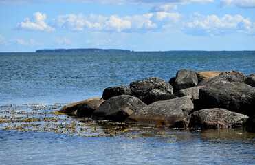Scenic view of a rocky coastline with large stones in the foreground and the calm blue sea stretching to the horizon under a partly cloudy sky. Perfect for themes of travel, nature, relaxation