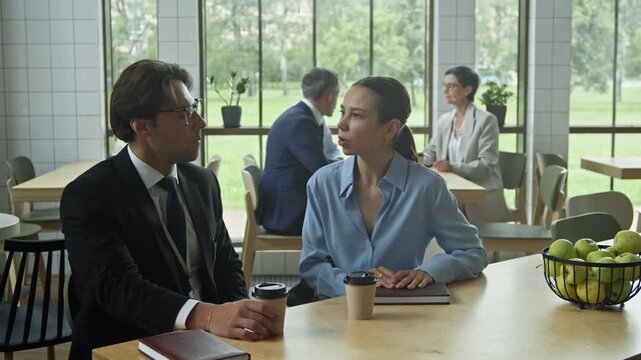 Young male and female colleagues in formalwear sitting by table in cafe, having coffee and talking about main points of report after conference or discussing new working ideas