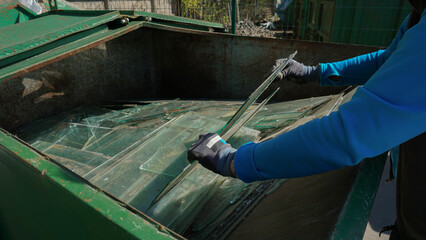 Hands in gloves disposing of old broken glass panes to waste containers in industrial recycling...