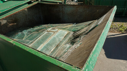 Hands in gloves disposing of old broken glass panes to waste containers in industrial recycling facility center. Processing recycled materials. Waste management, sustainability and safety 