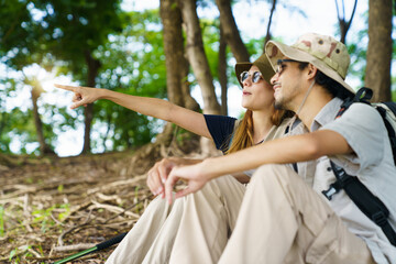 Man and woman hikers resting under tree near lake and meadow.
