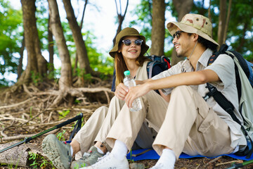 Man and woman hikers resting under tree near lake and meadow.