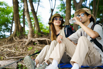 Man and woman hikers resting under tree near lake and meadow.