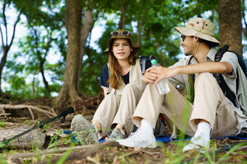 Man and woman hikers resting under tree near lake and meadow.