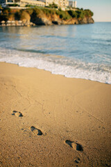 Footprints Leading to Ocean Waves on Sandy Beach