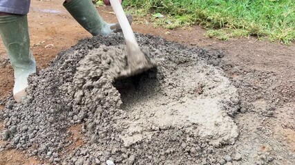 Close up of a construction worker mixing sand and cement manually with a hoe, creating mortar mixture for traditional building and construction work.