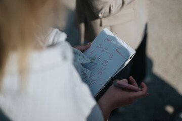 A close-up of an individual writing math equations in a notebook outside, showcasing creativity and...