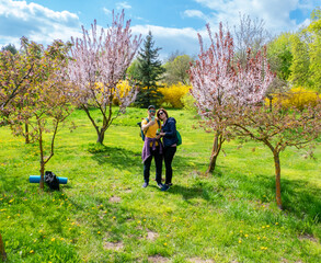 A cheerful couple takes a selfie amidst vibrant pink blooming trees and lush green grass in a beautiful spring park. Capturing happy moments on a sunny day surrounded by nature's beauty.