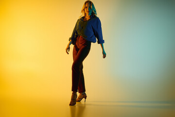 Fototapeta premium Stylish young woman poses confidently in trendy outfit against vibrant colored backdrop