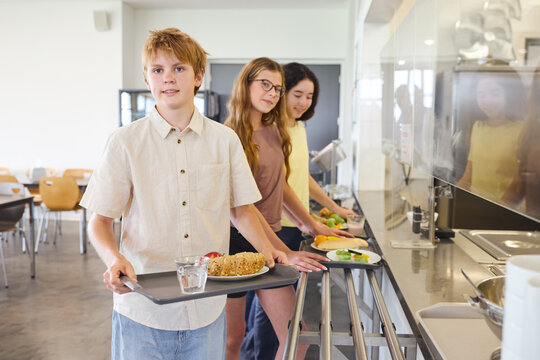Students standing in line in a school cafeteria with food trays