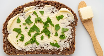 Top-down view of appetizing buttered dark bread with parsley and spreader
