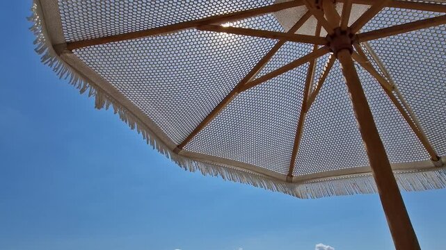 Beach umbrella with fringe. White knitted beach umbrella on a blue sky background. Close-up view from under a beach umbrella on a clear blue sky background. Concept of beach vacation, sea vacation