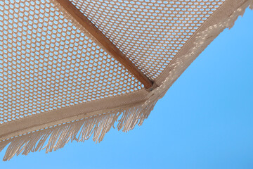 Beach umbrella with fringe. White knitted beach umbrella on a blue sky background. Close-up view...