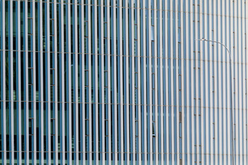 Close-up view of a modern building facade with vertical glass panels, creating an abstract striped pattern with repeating lines.