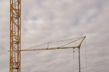 Yellow tower crane standing still under cloudy sky during construction