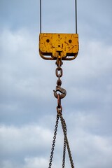 Crane hook hanging from chains on cloudy sky background
