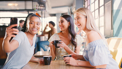 Group Of Female Friends Meeting Up In Restaurant Or Coffee Shop Taking Selfie On Mobile Phone