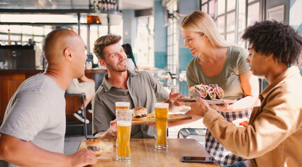 Group Of Male Friends Meeting Up In Bar Being Served Food By Waitress