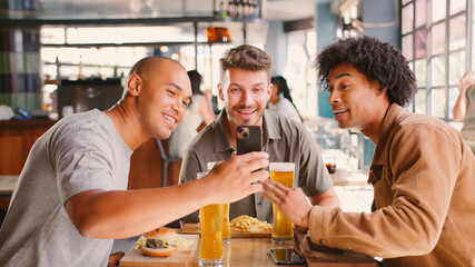 Group Of Male Friends Meeting Up In Bar Taking Photo With Food On Mobile Phone