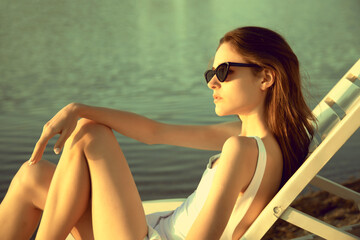 Young slim woman sunbathing wearing stylish sunglasses lies on chaise lounge near the ocean girl...