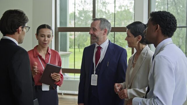 Young businesswoman with notepad introducing new financial expert or one of participants of international conference to colleagues while the man shaking hands of each employee