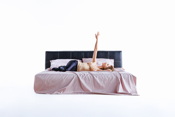 A woman is lying on a neatly made bed, stretching her arm toward the ceiling in a relaxed manner....