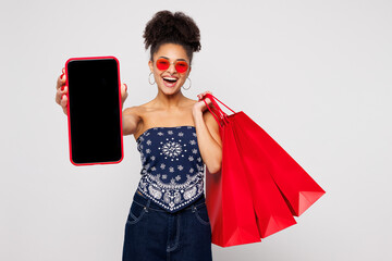 Young woman wears blue casual clothes hold in hand shopping red paper package bags use blank screen...